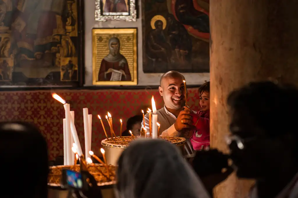 A father lifting his daughter to a candle stand inside the Church of the Nativity.