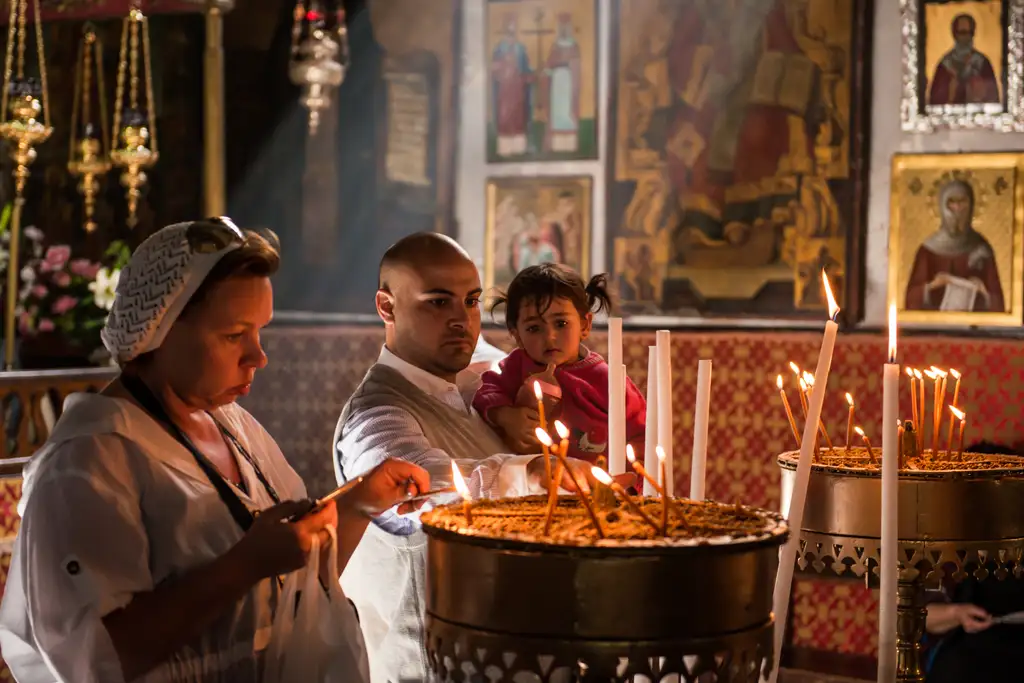 Pilgrims setting lit candles into the sand of a brass candle stand beneath the icons.