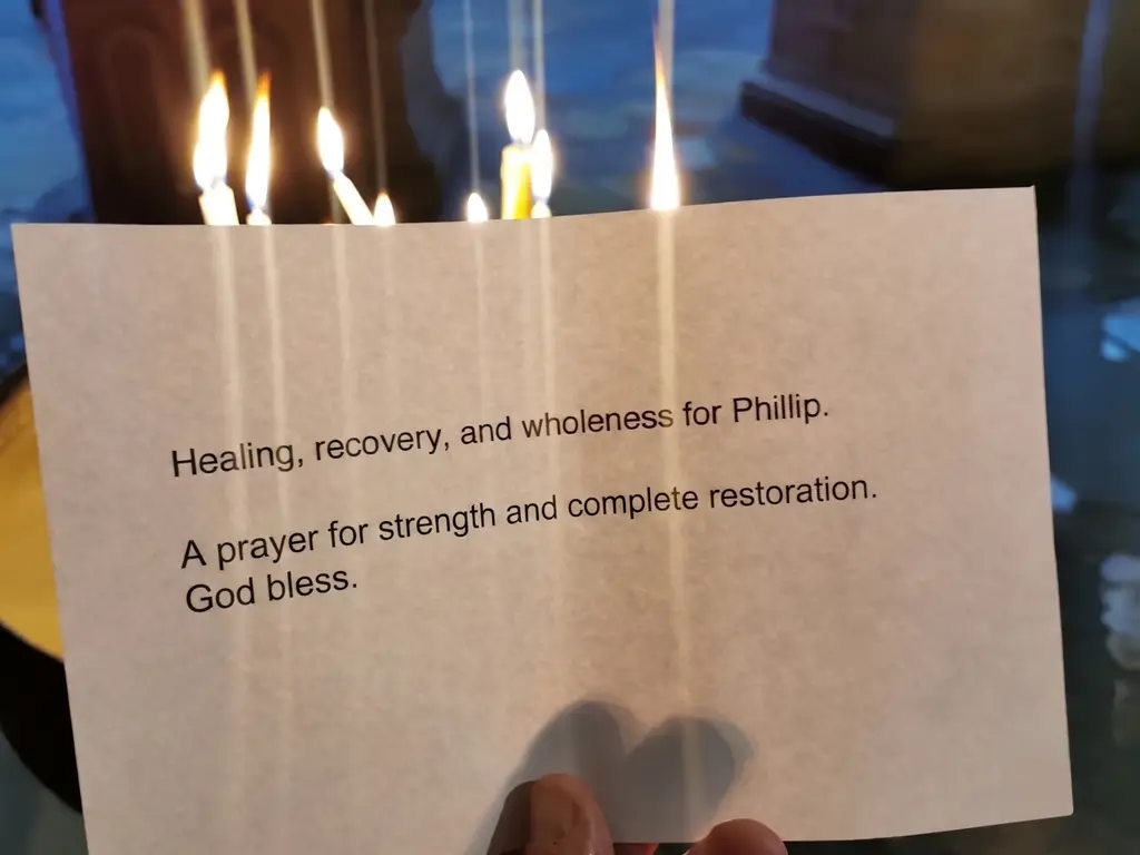 A printed intention card held up before rows of burning candles.